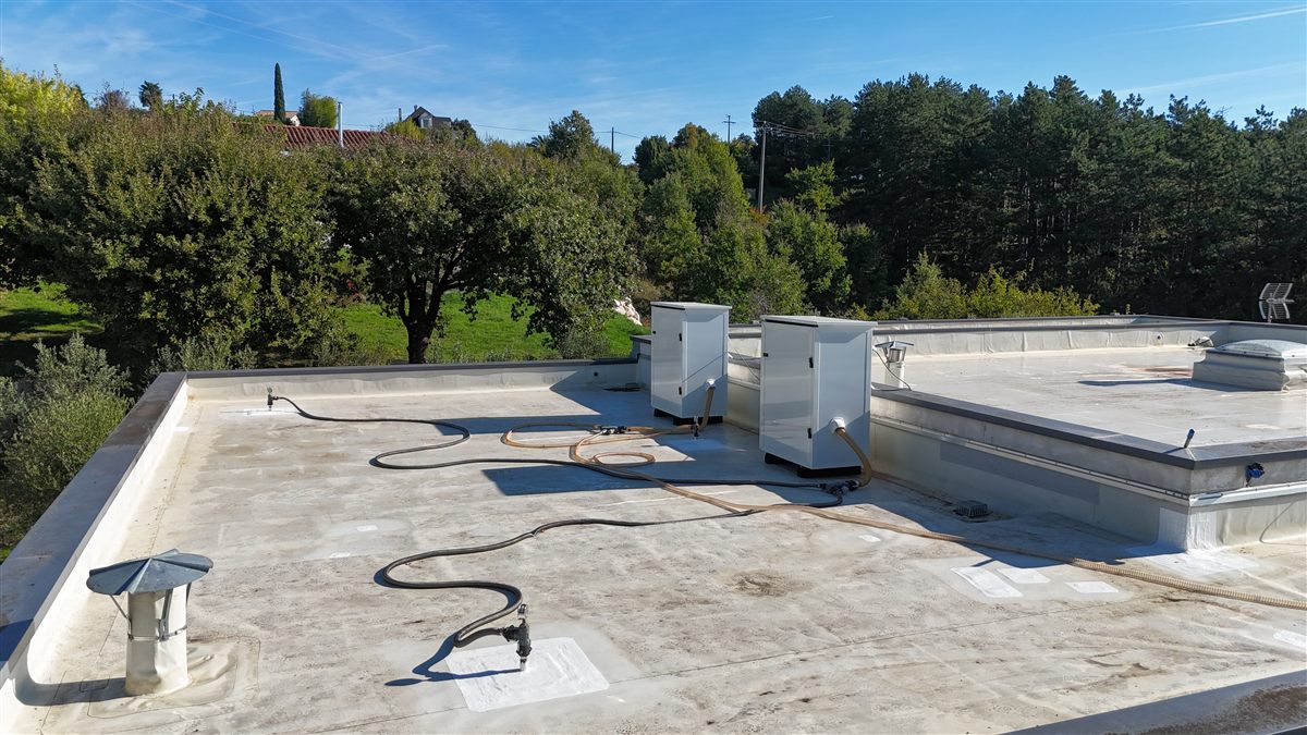 Vue d'ensemble d'une toiture-terrasse béton en cours d'assèchement, les flexibles courant sur la dalle.